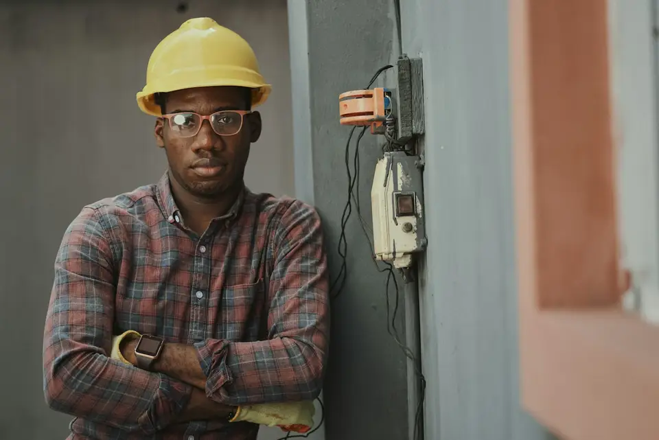 An electrician in a yellow hard hat working inside an open consumer unit.